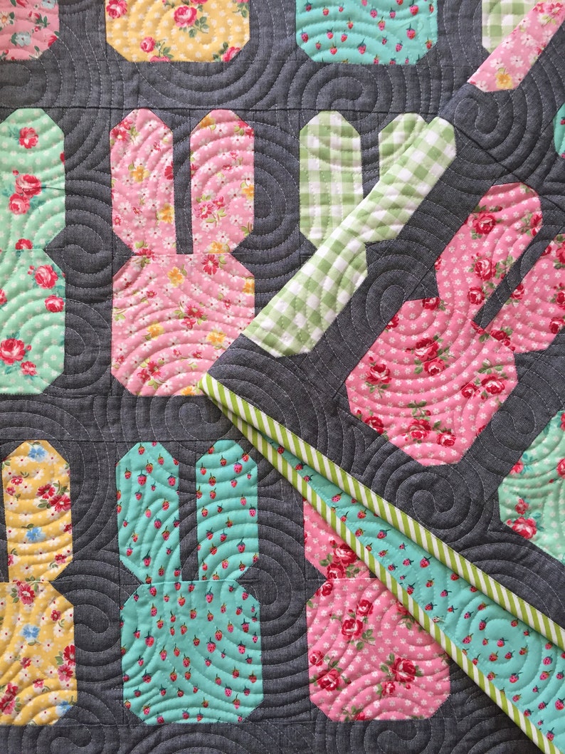 May include: A quilt with a patchwork design featuring bunny shapes in various floral prints. The quilt is made with a gray background and a green and white gingham border.