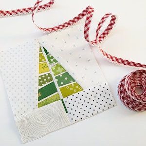 May include: A patchwork quilt block featuring a green and yellow Christmas tree design. The block is surrounded by white fabric with a small polka dot pattern and a white fabric with a small wave pattern. The block is bordered by a black and white polka dot fabric and a white fabric with a small cross pattern.