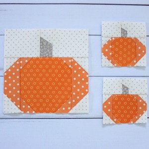 May include: Three fabric pumpkin squares in different sizes. The largest pumpkin is orange with white polka dots and a gray stem. The two smaller pumpkins are orange with a white floral pattern and gray stems.
