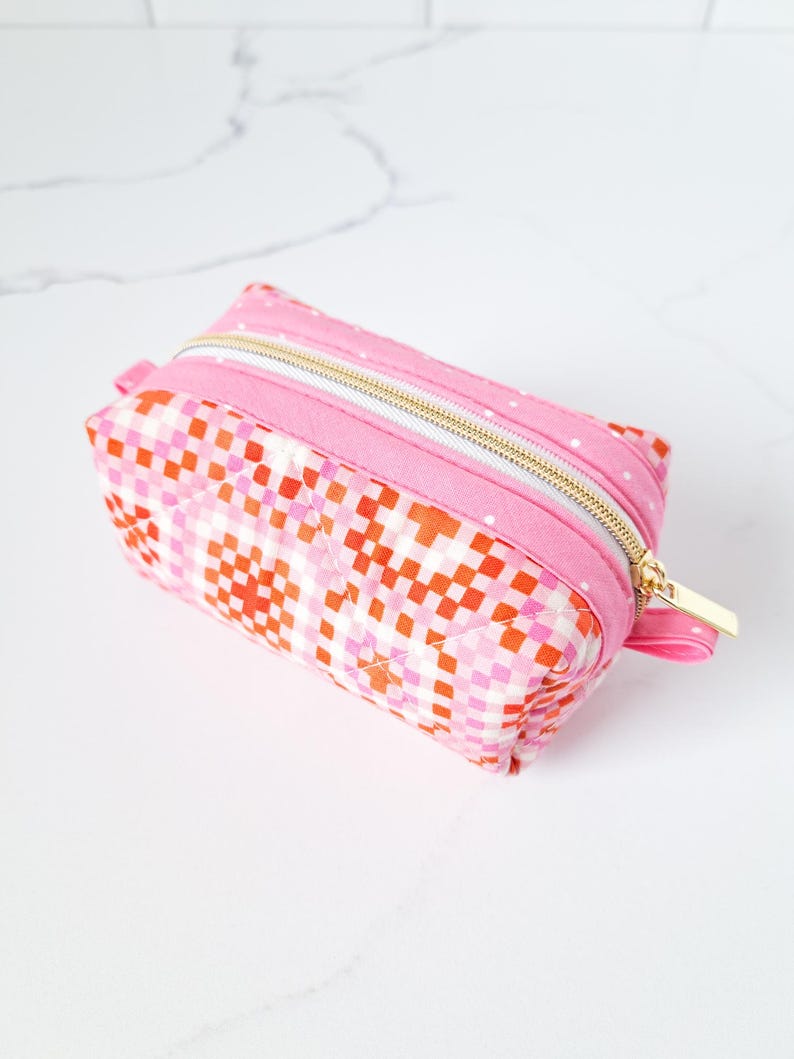May include: A pink and orange quilted makeup bag with a gold zipper.