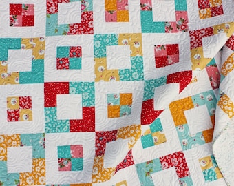 May include: A quilt with a patchwork design featuring squares of red, yellow, turquoise, and white fabric. The quilt is made with a variety of floral prints and has a white background.