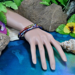 May include: Two colorful bangle bracelets with floral patterns in shades of blue, red, and white. The bracelets are stacked on a mannequin's wrist.