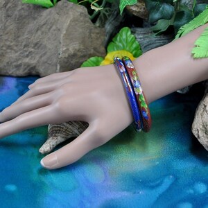 May include: Two enamel bangles with floral designs. One bangle is blue with white flowers and the other is red with white flowers.