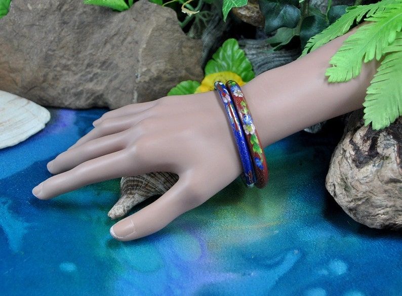May include: Two enamel bangles with floral designs. One bangle is blue with white flowers and the other is red with white flowers.