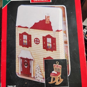 May include: A Hallmark Keepsake Ornament box featuring a miniature house with a red roof and shutters, and a small rocking chair ornament. The box is red and black, with text that reads "The Night Before Christmas."