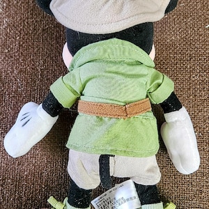 Puede incluir: Un peluche de Mickey Mouse con un atuendo de safari. El juguete tiene orejas negras, un sombrero de safari beige, una camisa verde con cintur&oacute;n marr&oacute;n y pantalones cortos color caqui. Los zapatos son marrones con cordones verdes.