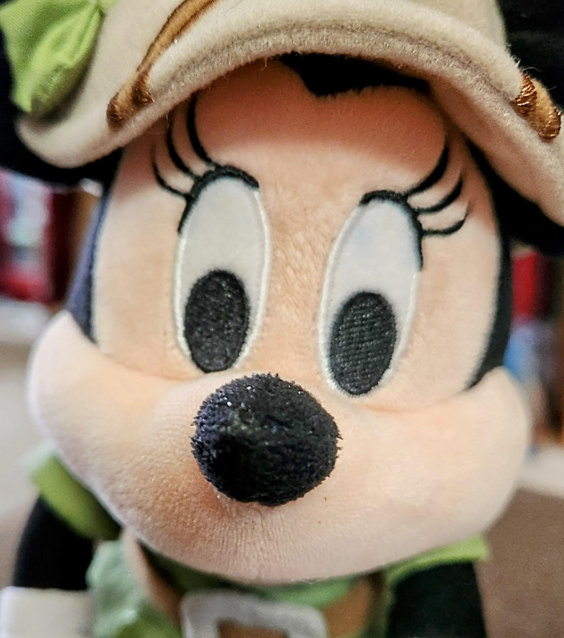 Puede incluir: Mu&ntilde;eca de peluche de Minnie Mouse con un sombrero de estilo safari con un lazo verde y un atuendo verde y blanco. La mu&ntilde;eca tiene ojos grandes y expresivos, una nariz negra y orejas negras. Es un objeto de colecci&oacute;n.