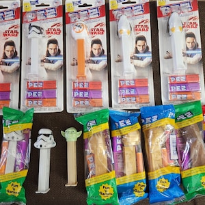 May include: A collection of Star Wars PEZ dispensers and candy refills. The dispensers feature characters like a Stormtrooper, Yoda, and BB-8. The packaging includes the Star Wars logo and images of Rey.