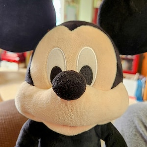 Peut inclure: Peluche de Mickey Mouse avec une t&ecirc;te, des oreilles et des bras noirs, un visage beige et un nez noir. Le jouet a des yeux blancs et un corps rouge et noir. Un personnage Disney classique.