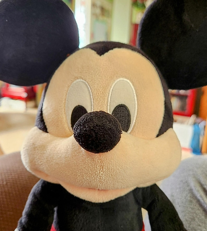 Peut inclure: Peluche de Mickey Mouse avec une t&ecirc;te, des oreilles et des bras noirs, un visage beige et un nez noir. Le jouet a des yeux blancs et un corps rouge et noir. Un personnage Disney classique.