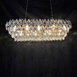 May include: A rectangular chandelier with multiple tiers of sparkling crystal droplets. The fixture is suspended from the ceiling by chains and emits a warm, inviting glow. The crystals reflect light, creating a dazzling display.
