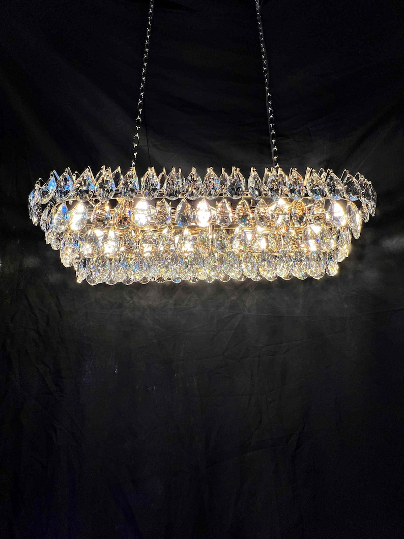 May include: A rectangular chandelier with multiple tiers of sparkling crystal droplets. The fixture is suspended from the ceiling by chains and emits a warm, inviting glow. The crystals reflect light, creating a dazzling display.