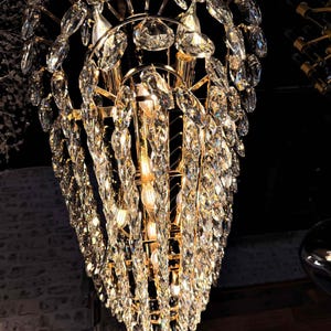 May include: A glamorous chandelier with a gold-toned frame and cascading crystal accents. The crystals are multifaceted, reflecting light and creating a dazzling display. The fixture is suspended from the ceiling, adding a touch of luxury to the space.