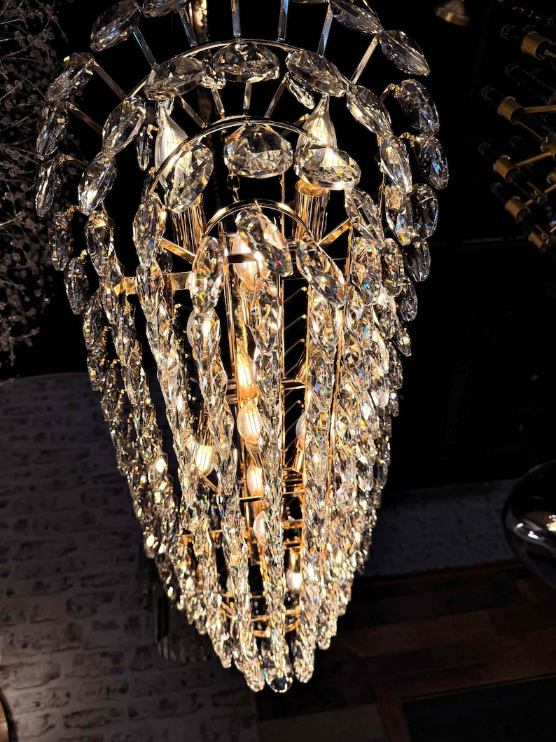 May include: A glamorous chandelier with a gold-toned frame and cascading crystal accents. The crystals are multifaceted, reflecting light and creating a dazzling display. The fixture is suspended from the ceiling, adding a touch of luxury to the space.