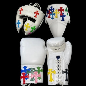May include: White boxing gear set, including a head guard, shorts, and gloves. The set features colorful cross designs in red, blue, yellow, green, and pink. The gloves are labeled "10 OZ".