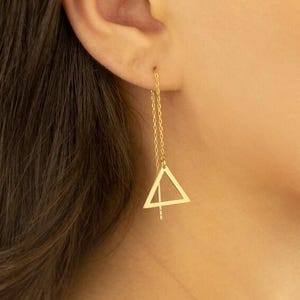 Può includere: Orecchini a catena color oro con un design a triangolo geometrico. Gli orecchini presentano una delicata catena che pende dall'orecchio, con un ciondolo a triangolo sospeso in basso. Il triangolo ha una linea nel mezzo. Un accessorio semplice ed elegante.