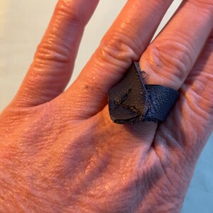 May include: A dark blue leather ring with a pointed end. The ring is worn on a finger.
