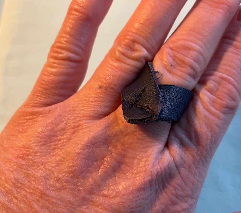 May include: A dark blue leather ring with a pointed end. The ring is worn on a finger.
