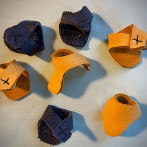 May include: Six leather finger thimbles, three are yellow and three are dark blue. Each thimble has a small cross stitched on it.