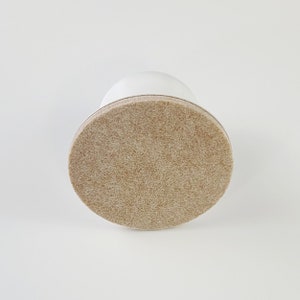 May include: A white furniture leg with a beige felt pad on the bottom.