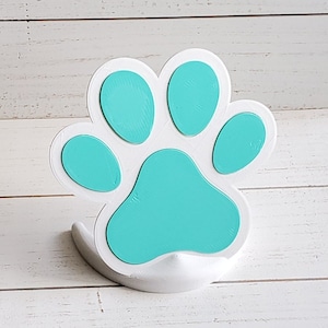 May include: White ceramic paw print with a teal blue paint finish. The paw print is three-dimensional and has a raised base.