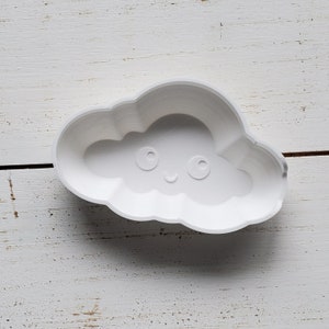Puede incluir: Molde de plástico blanco en forma de nube con una cara sonriente y dos ojos.