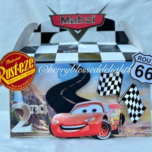 Może przedstawiać: Ozdobione pudełko na upominki z czerwonym samochodem wyścigowym, znakiem Route 66 i szachownicami. Pudełko ma czarno-białą szachownicę na górze i tło z drogą oraz napisem "2nd". Pudełko ma również imię "Mahzi".