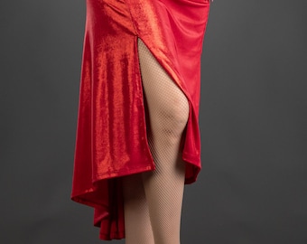 May include: A striking red dress with long sleeves and a high slit, featuring a ruched side detail. The outfit includes nude fishnet stockings and high-heeled sandals. The fabric has a shimmering, reflective finish.