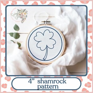 Może przedstawiać: Obręcz do haftu o średnicy 10 cm z białym tłem z tkaniny i niebieskim konturem koniczyny. Tekst "4" shamrock pattern" znajduje się pod obręczą.