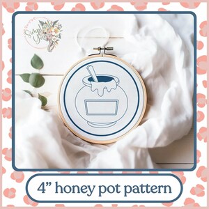 Może przedstawiać: Obręcz do haftu o średnicy 10 cm z białym tłem z tkaniny. Obręcz zawiera niebieski rysunek liniowy garnka miodu z chochlą w środku. Tekst "4" honey pot pattern" znajduje się pod obręczą.