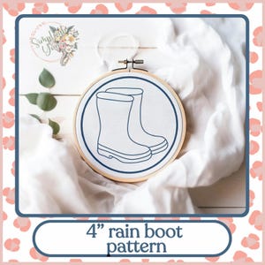 May include: A 4" rain boot embroidery pattern in a wooden embroidery hoop on a white fabric background.