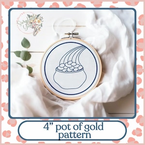 May include: A 4-inch embroidery hoop with a white fabric background. The fabric is embroidered with a blue outline of a pot of gold with a rainbow pouring gold coins into the pot.