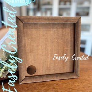 Op de afbeelding: Een vierkant houten frame met een donkerbruine afwerking. Het frame heeft een cirkelvormig gat linksonder en de tekst "Easely Created" is zichtbaar. De woorden "Digital Cut File" zijn ook zichtbaar.