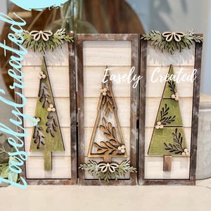 May include: Three wooden Christmas tree decorations with a rustic aesthetic. Each tree is a different design, painted green and brown, and set against a white background. The text "Easely Created" is visible on the decorations and in a blue circle.