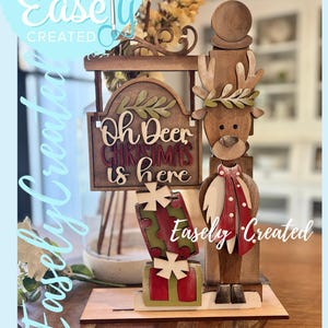 May include: Wooden Christmas decoration featuring a reindeer with a sign that reads "Oh Deer Christmas is here." The decoration includes gift boxes and is labeled "Easely Created."
