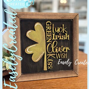 Peut inclure: Panneau encadré en bois avec un trèfle doré et les mots "Luck Irish Clover Wish Green Kiss" sur fond noir. Le panneau comprend également le texte "Easely Created" et "Digital Cut File".