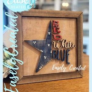 Peut inclure: Panneau encadré en bois avec une étoile bleue et les mots "Red White Blue". Le panneau comprend également le texte "Easely Created" et "Digital Cut File".