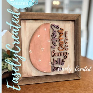 Peut inclure: Panneau en bois sur le thème de Pâques avec un cadre marron. Le panneau présente un demi-œuf rose peint avec des points blancs et les mots "Easter, Carrot, Bunny, Jelly" en lettrage coloré. Le texte "Easely Created" est également visible.