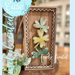 May include: Wooden framed wall art with three shamrock cutouts in green and yellow. The frame has a decorative border and a rustic wood-grain background. The text "Digital Cut File Easely Created" is visible.