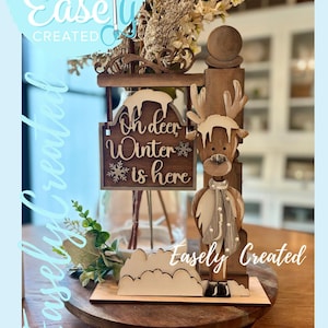 May include: A wooden winter-themed decoration featuring a reindeer figure and a sign that reads "Oh deer Winter is here." The sign and reindeer are light brown with white accents. The words "Digital Cut File" and "Easely Created" are also visible.