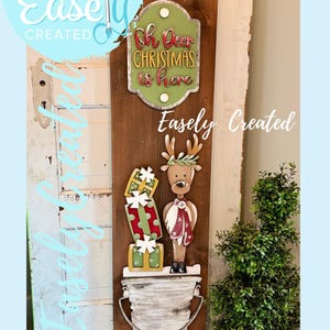 May include: Wooden Christmas sign with a reindeer, presents, and the text "Oh Deer Christmas is here." The sign is brown with green, red, and white accents. The words "Easely Created" are also visible.