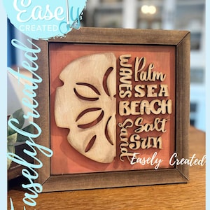 May include: Wooden framed wall art with a sand dollar design and the words "Waves, Palm, Sea, Beach, Salt, Sun". The text "Easely Created" is also visible. The background is coral-colored.