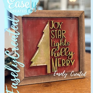Peut inclure: Panneau de Noël encadré avec un fond rouge et un sapin de Noël doré. Le panneau indique "JOY STAR Lights holly MERRY" en lettres dorées. Le texte "Easely Created" est également visible.