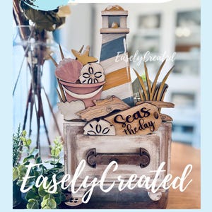 Puede incluir: Decoración de madera con temática de playa que presenta un faro, conchas marinas y un cubo. El diseño incluye el texto "Seas the day" en un letrero de madera. También son visibles las palabras "Instant Digital Download".