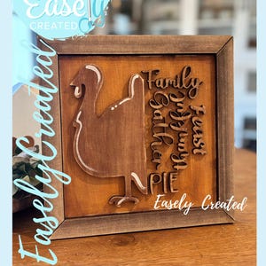 Peut inclure: Panneau en bois encadré avec une silhouette de dinde et les mots "Family, Gather, Feast, Pie" dans une police décorative. Le panneau comprend également le texte "Easely Created" et "Digital Cut File". La dinde est marron avec des accents blancs.