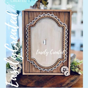 Op de afbeelding: Houten verwisselbaar frame voor "Table Top Easel" inzetstukken. Het frame heeft een lichte houtnerf achtergrond met een decoratieve witte kantachtige rand. De tekst "Easely Created" is zichtbaar.