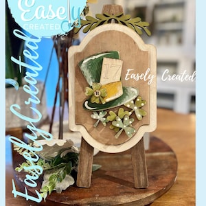 May include: Wooden St. Patrick's Day sign on a small easel. The sign features a green top hat, shamrocks, and the number 17. The words "Easely Created" are written on the sign and around the image.
