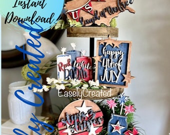 May include: A three-tiered wooden tray decorated with red, white, and blue patriotic themed cutouts. The top tier features a cutout of the United States with the text "Land of the Free". The middle tier features a cutout with the text "Red White Boom" and a cutout with the text "Happy 4th of July". The bottom tier features a cutout with the text "Stars & Stripes".