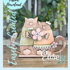 May include: A digital cut file of two cats holding a flower. The cats are brown and white with pink accents. The file is for instant download and is created by Easley Created.