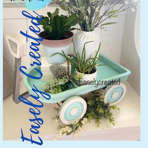 Op de afbeelding: Een lichtblauwe houten wagen met witte wielen en een wit en bruin houten handvat. De wagen is gevuld met potplanten, waaronder een cactus, een aloëplant en een boeket witte bloemen. De wagen staat op een houten oppervlak. De tekst "Easlycreated" is zichtbaar op de wagen.